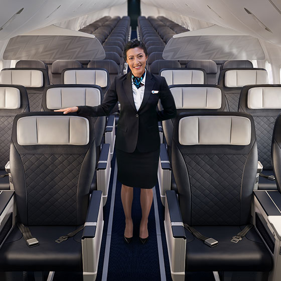 Un agent de bord de WestJet se tient debout dans l’allée de la cabine Privilège dotée de sièges en configuration 2x2.