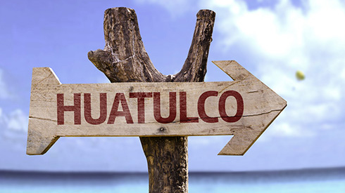 Wooden sign that reads Huatulco pointing to a beach