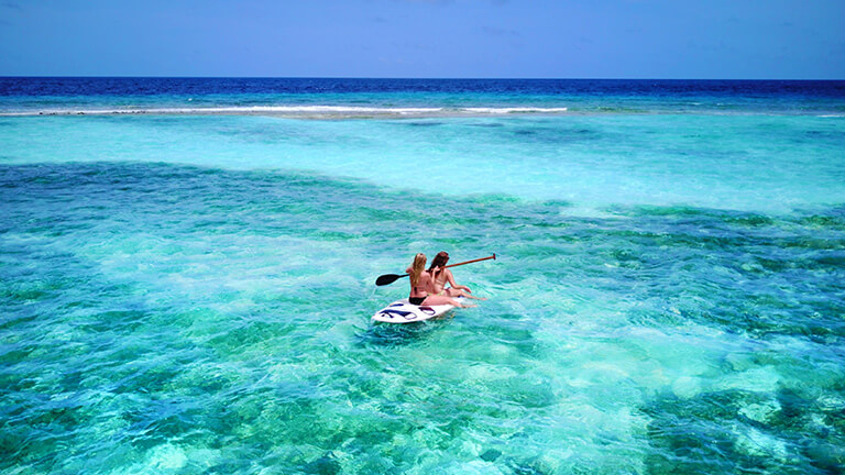 Des amis assis sur une planche à pagaie naviguant sur des eaux turquoise. 